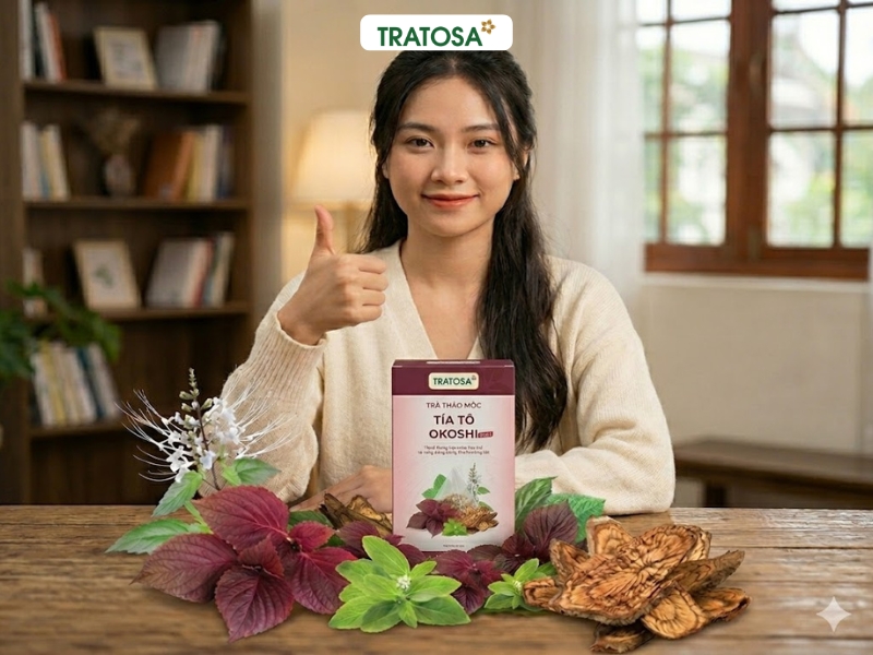 Hộp trà tía tô Okoshi Plus Tratosa chính hãng trên nền gỗ, bên cạnh là một ly trà tía tô nóng hổi và những lá tía tô tươi, thể hiện sự tự nhiên và chất lượng của sản phẩm.