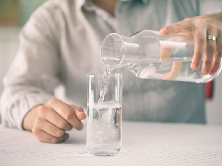Người tiểu đường nên uống gì thay nước ngọt? 7 lựa chọn dễ áp dụng Người đang rót nước lọc từ bình thủy tinh vào ly.